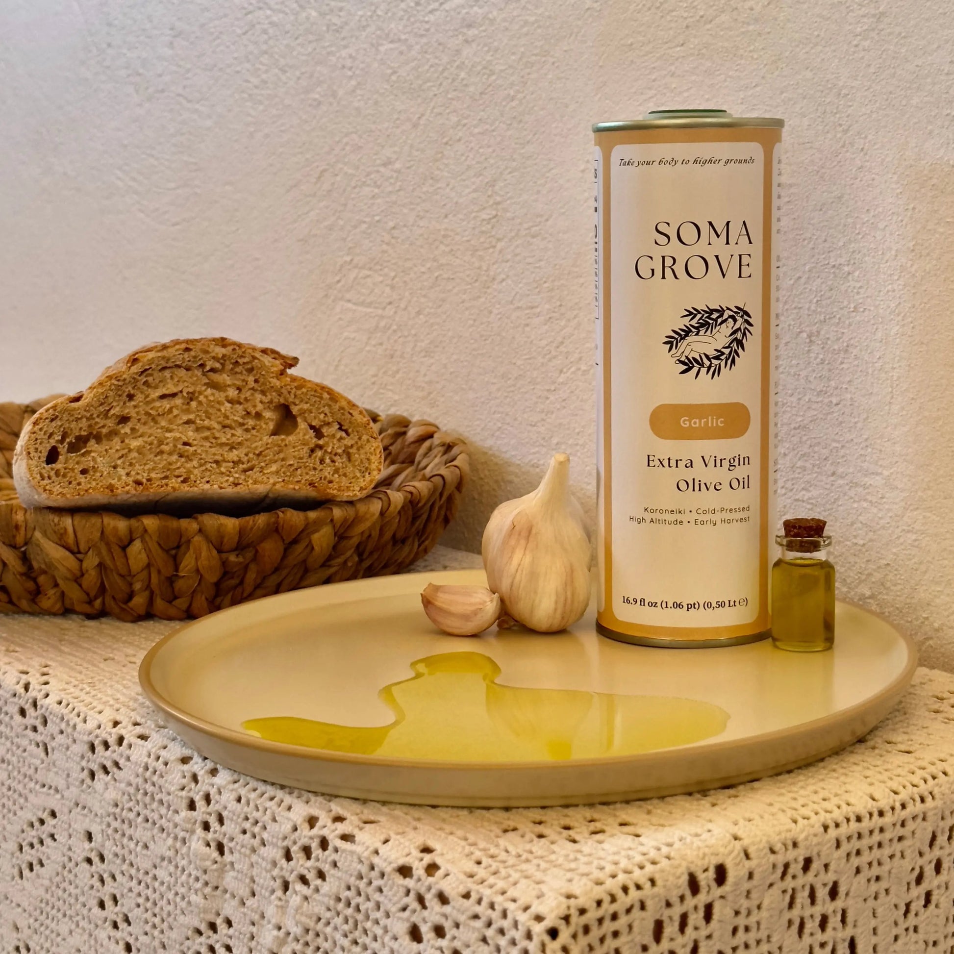 Soma Grove Garlic olive oil can with bread and garlic on a textured surface.