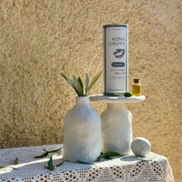 Soma Grove olive oil bottle on a small white table with a textured beige wall background