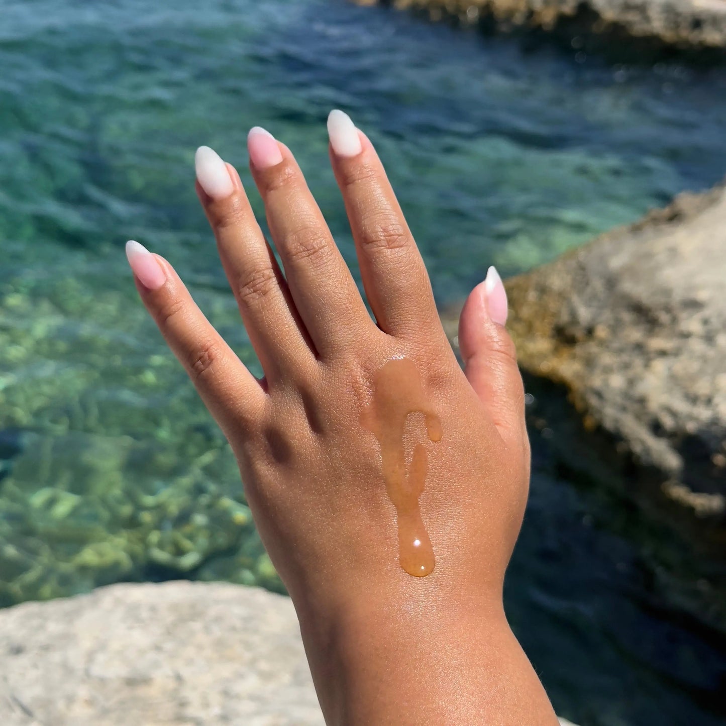 Hand with a small amount of Soma Grove Apothecary Oil on it against a natural background.