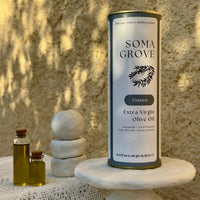 An outdoor setting with traditional Greek textiles and stone surfaces, featuring Classic Extra Virgin Olive Oil by Soma Grove.