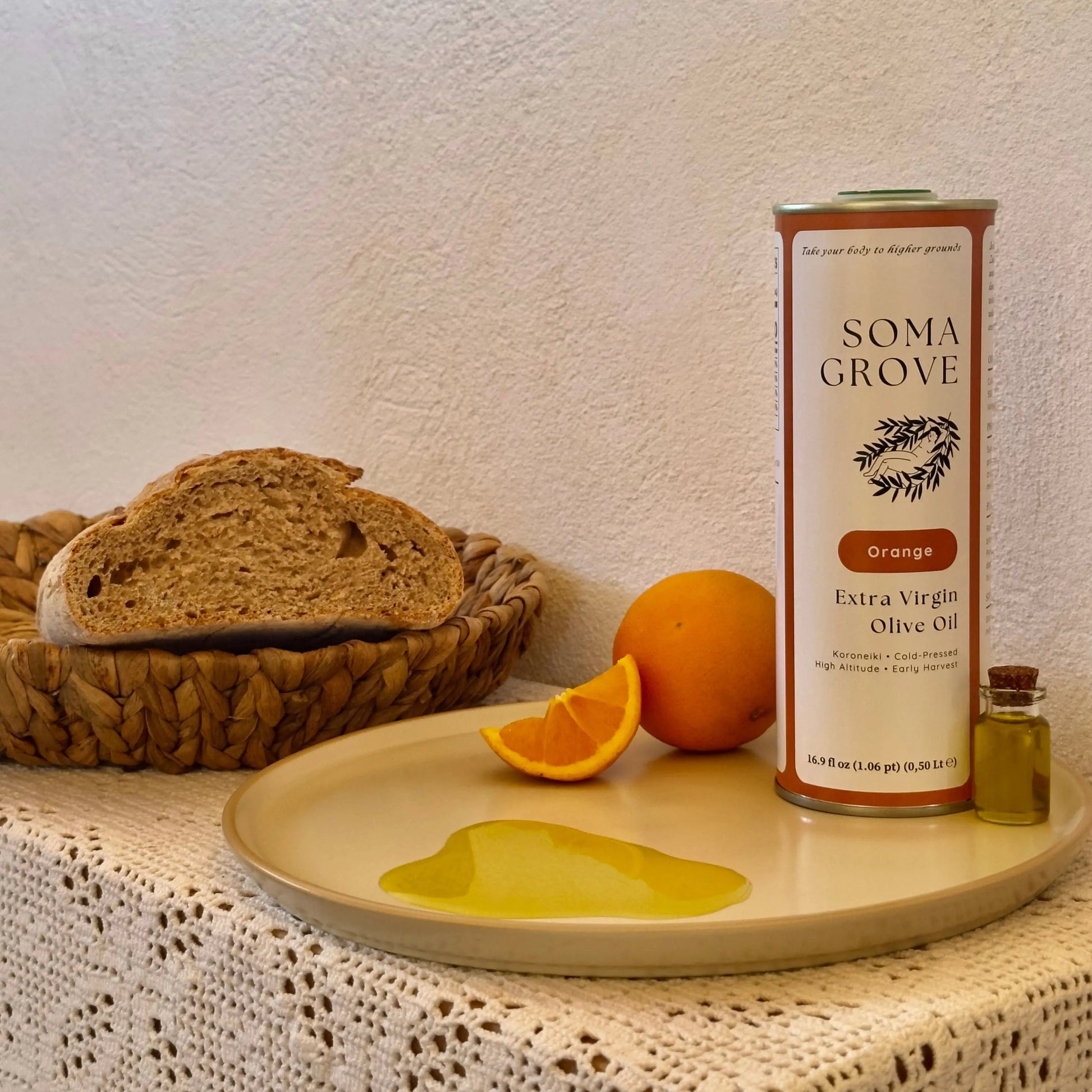 Soma Grove Orange Extra Virgin Olive Oil bottle on a table with bread and oranges.